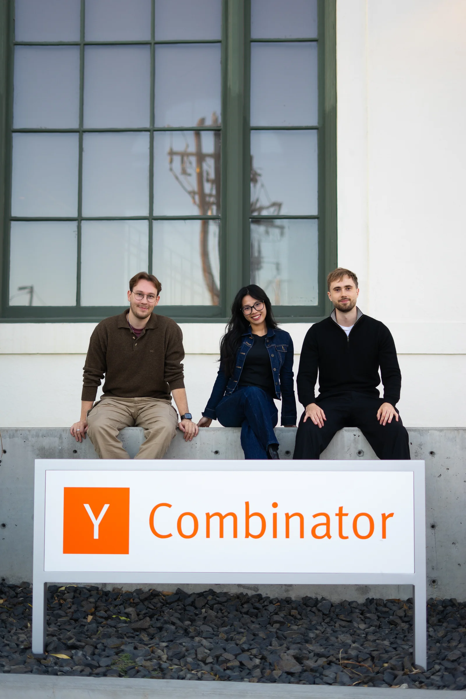 Ordo's founders, left to right Adam Tovatt, Kristina Hoang and Sebastian Apelgren, sitting on a concrete ledge above a Y Combinator sign, looking at the camera.